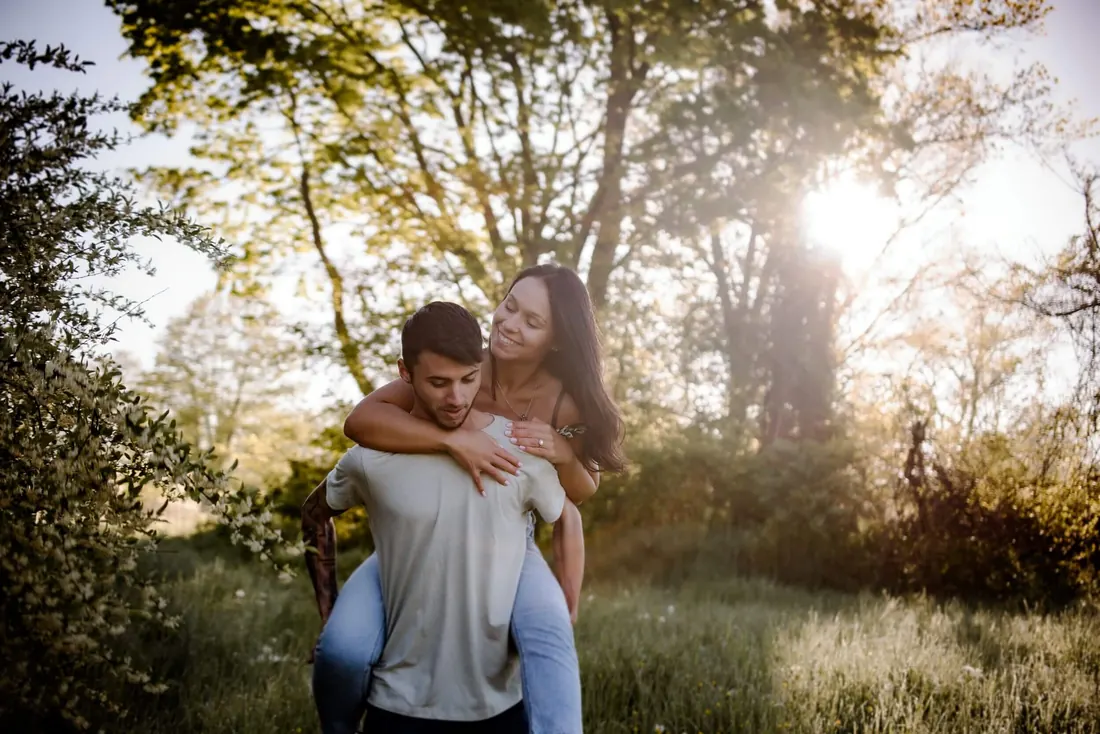 A couple laughing in backlit golden light, one carrying the other