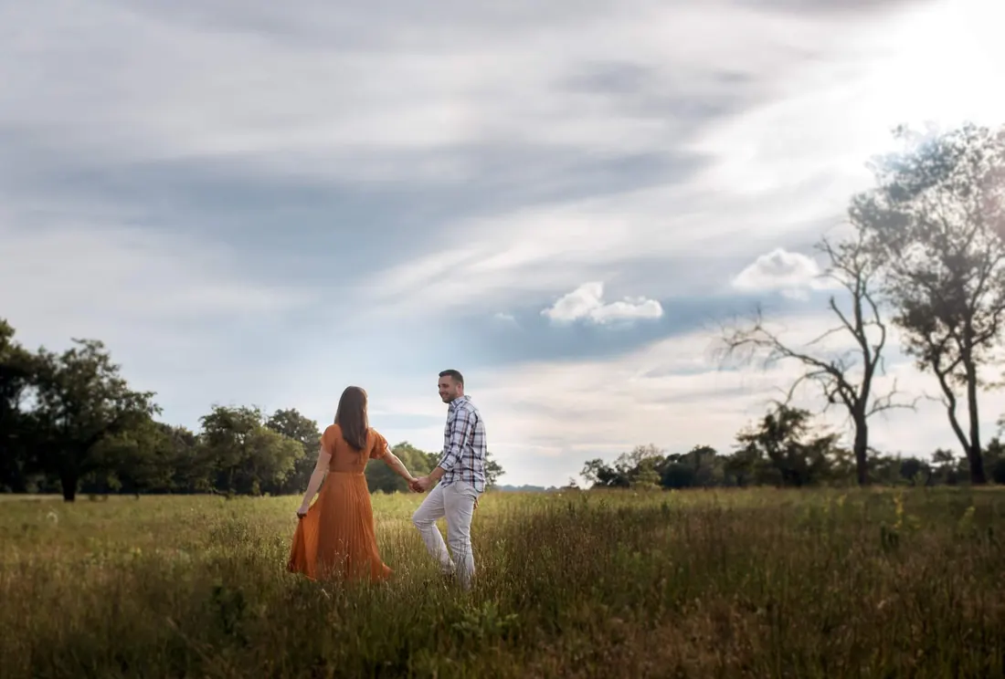 A couple walking through a field under a wide sky