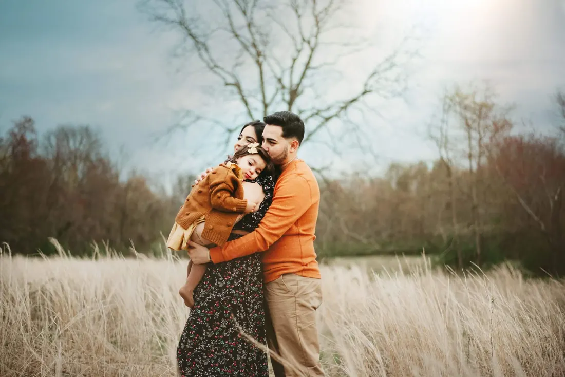 A family standing in an open field, father holding the baby