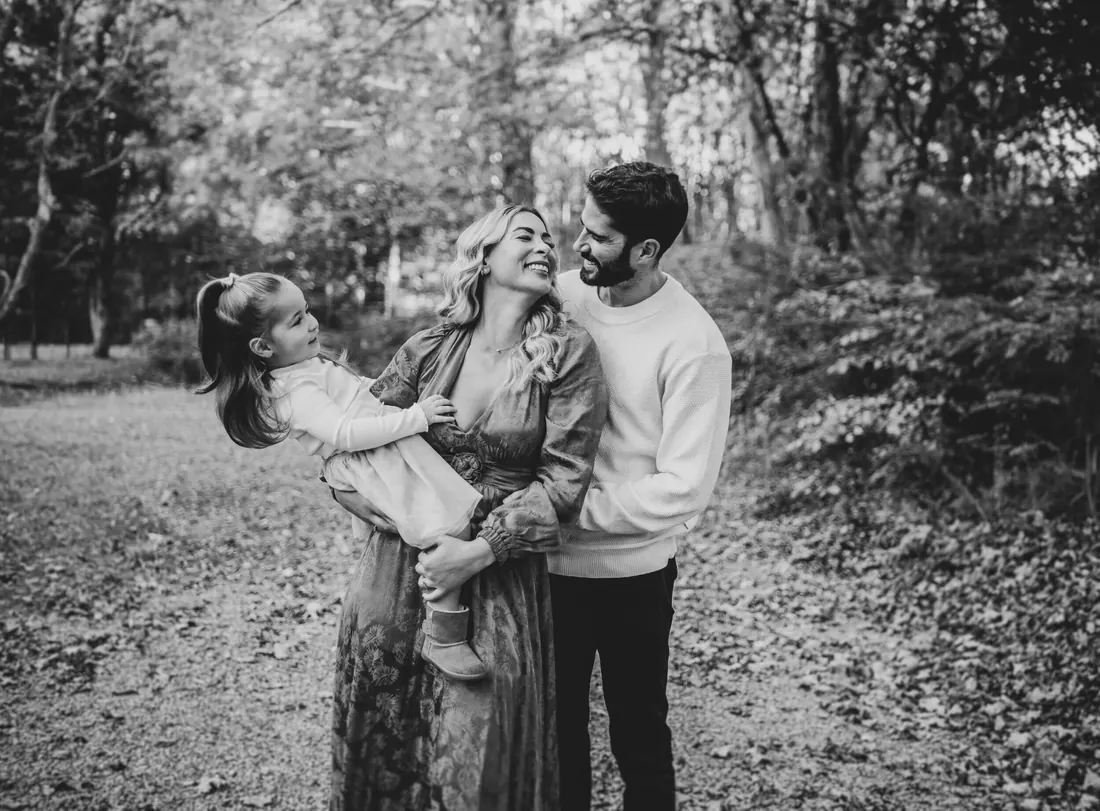 Black and white photograph of parents laughing with their daughter in the woods