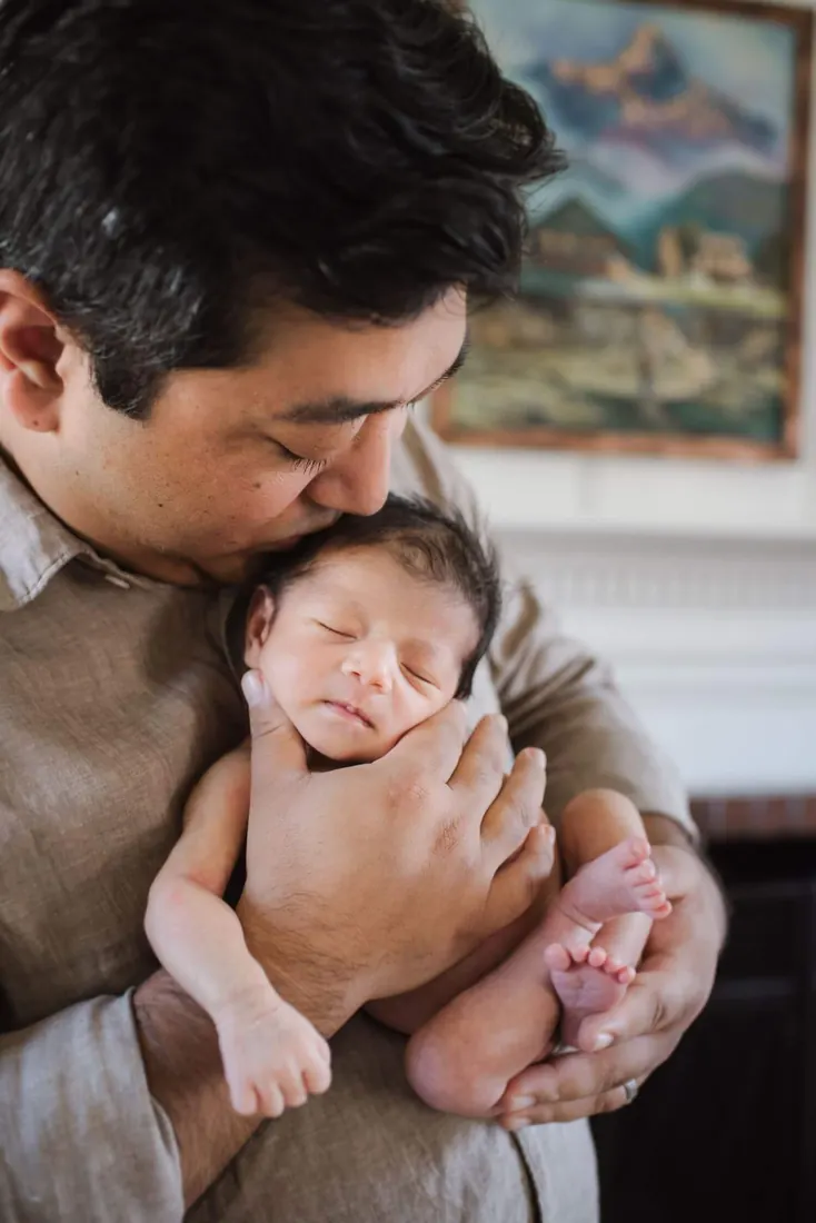 A father holding and kissing his newborn at home