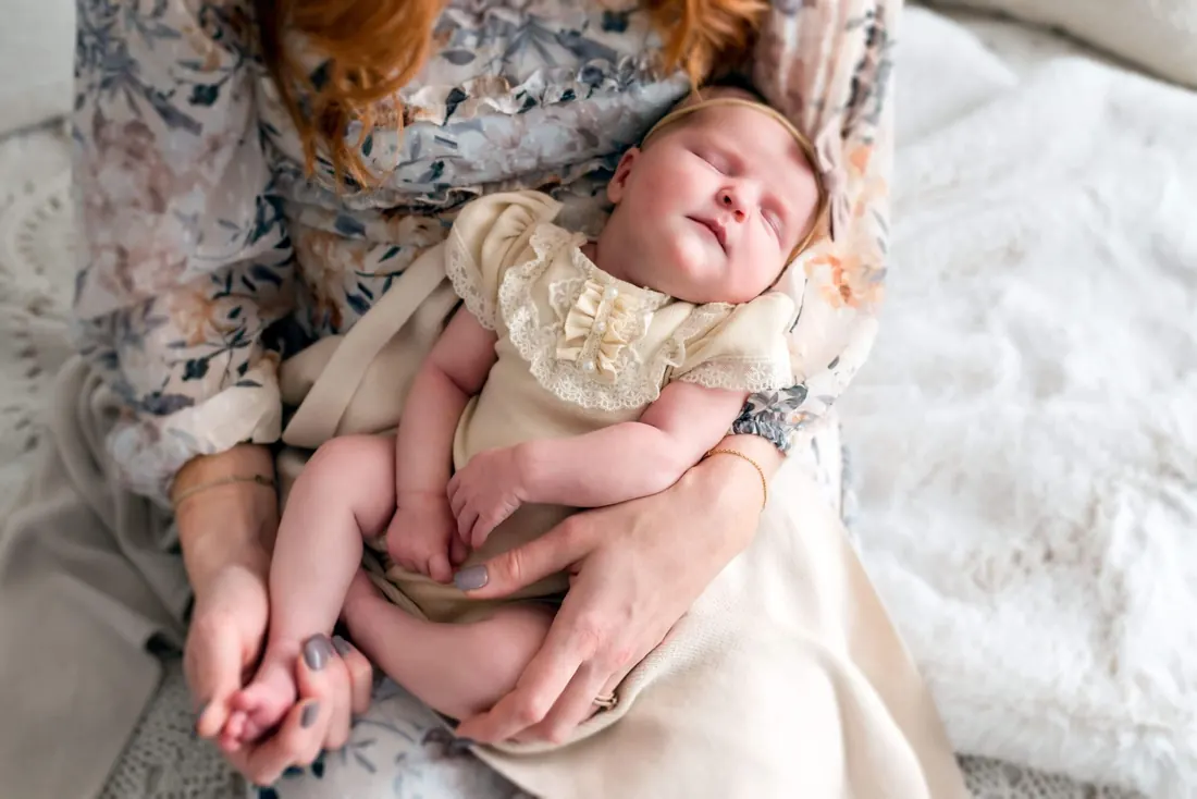 A newborn asleep on her mother’s lap in a floral dress
